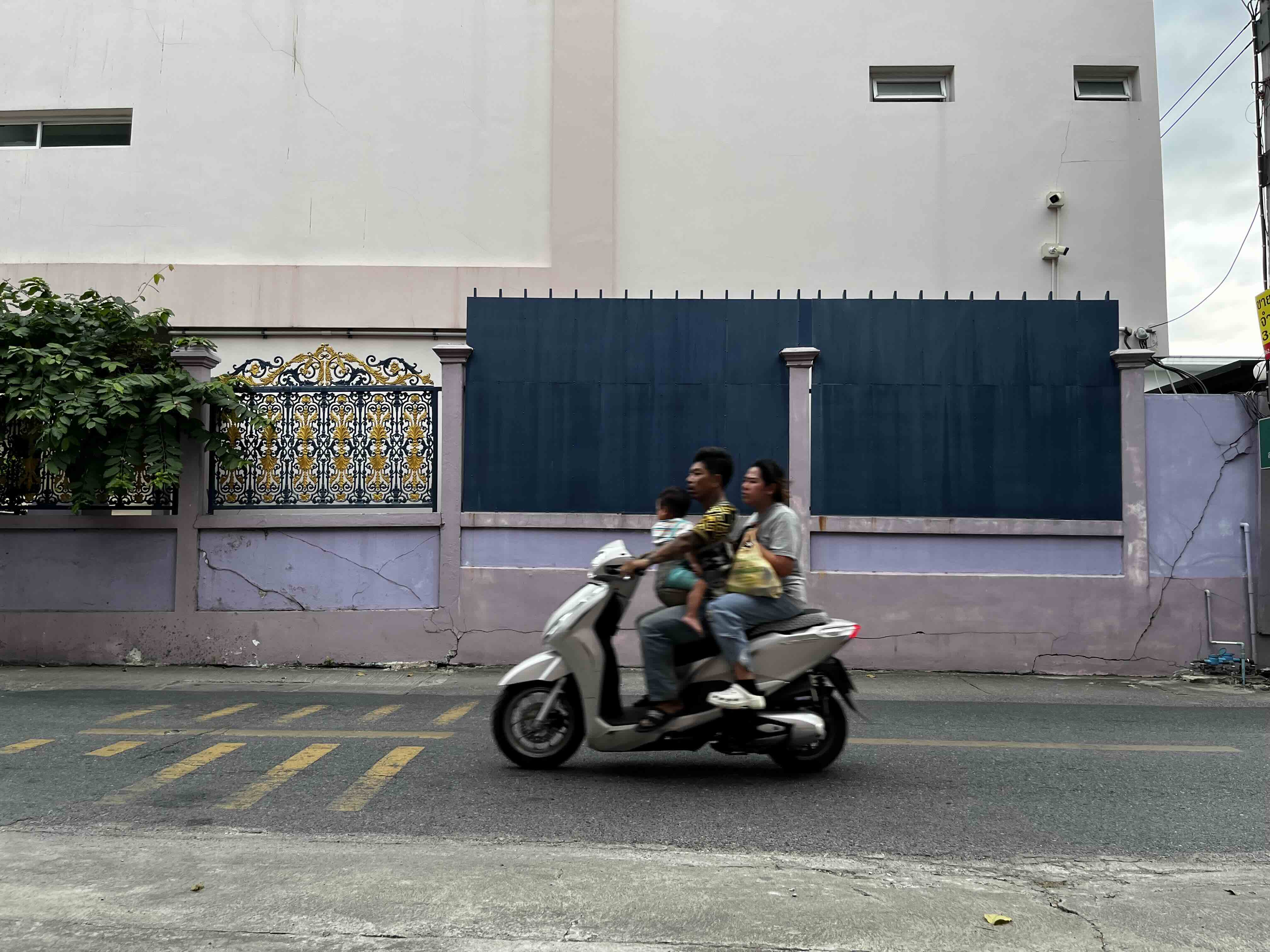 Riders on a white scooter passing a wall in Thailand